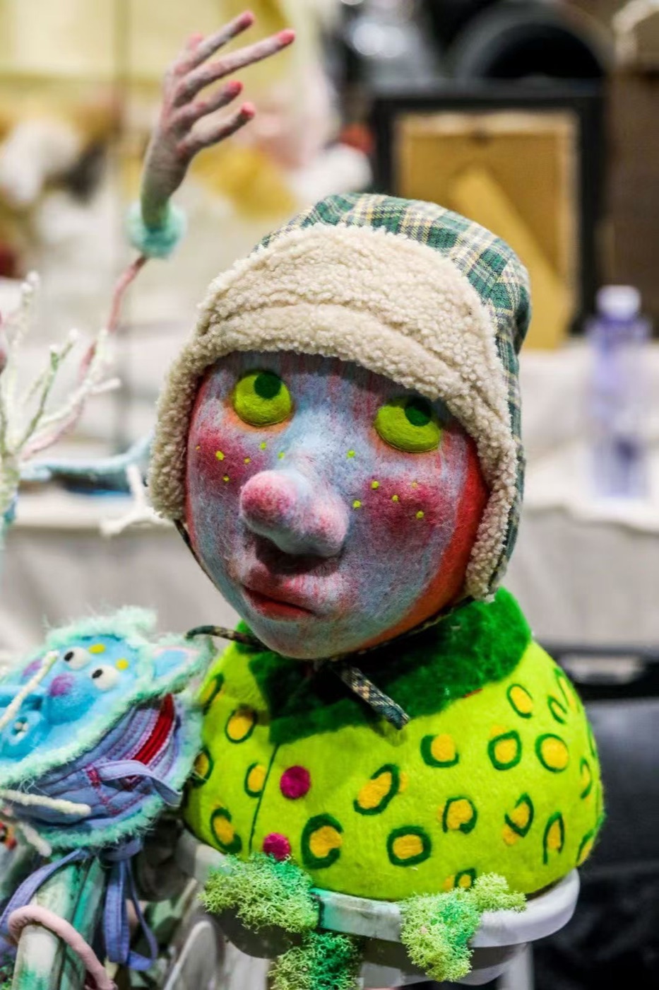 Archive creature with green eyes, checked cap, and bright textile body.
