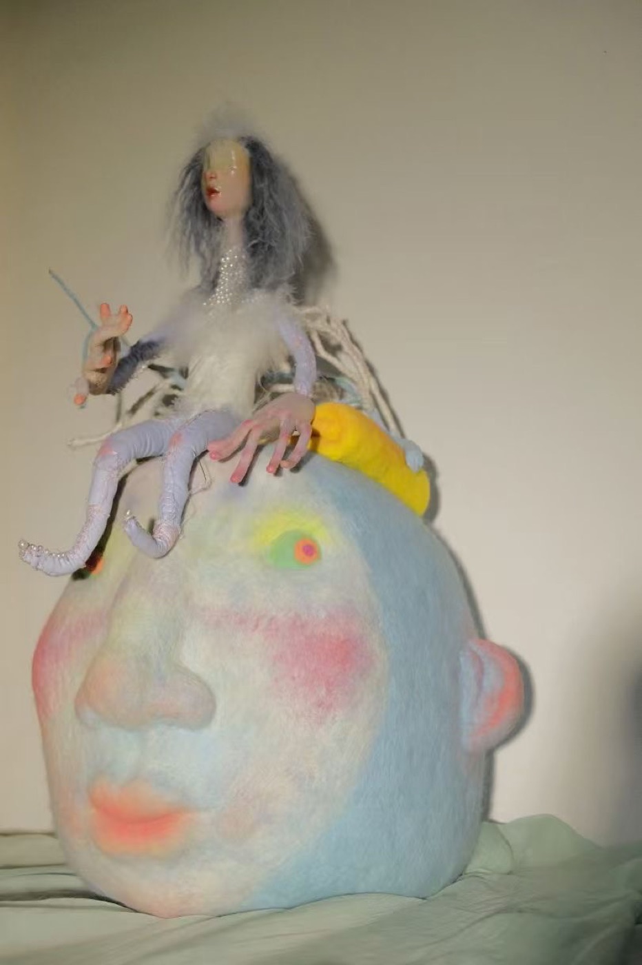 Past soft sculpture with small figure seated on a large pale blue head form.