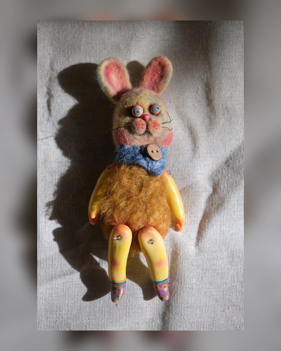 Tick Tock, a made-to-order handmade wool rabbit art doll with colorful eyes, yellow jointed legs, and a blue textile collar.