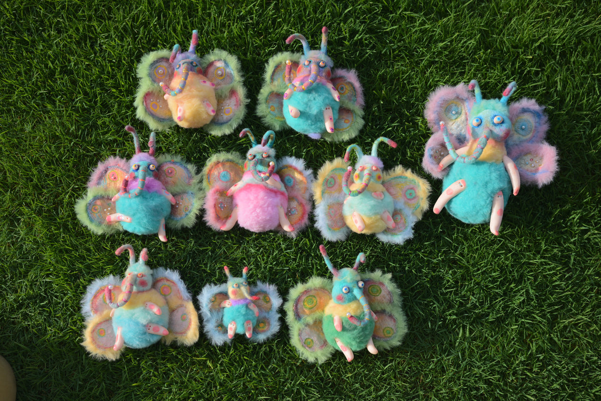 A group of handmade colorful wool moth characters arranged on grass.