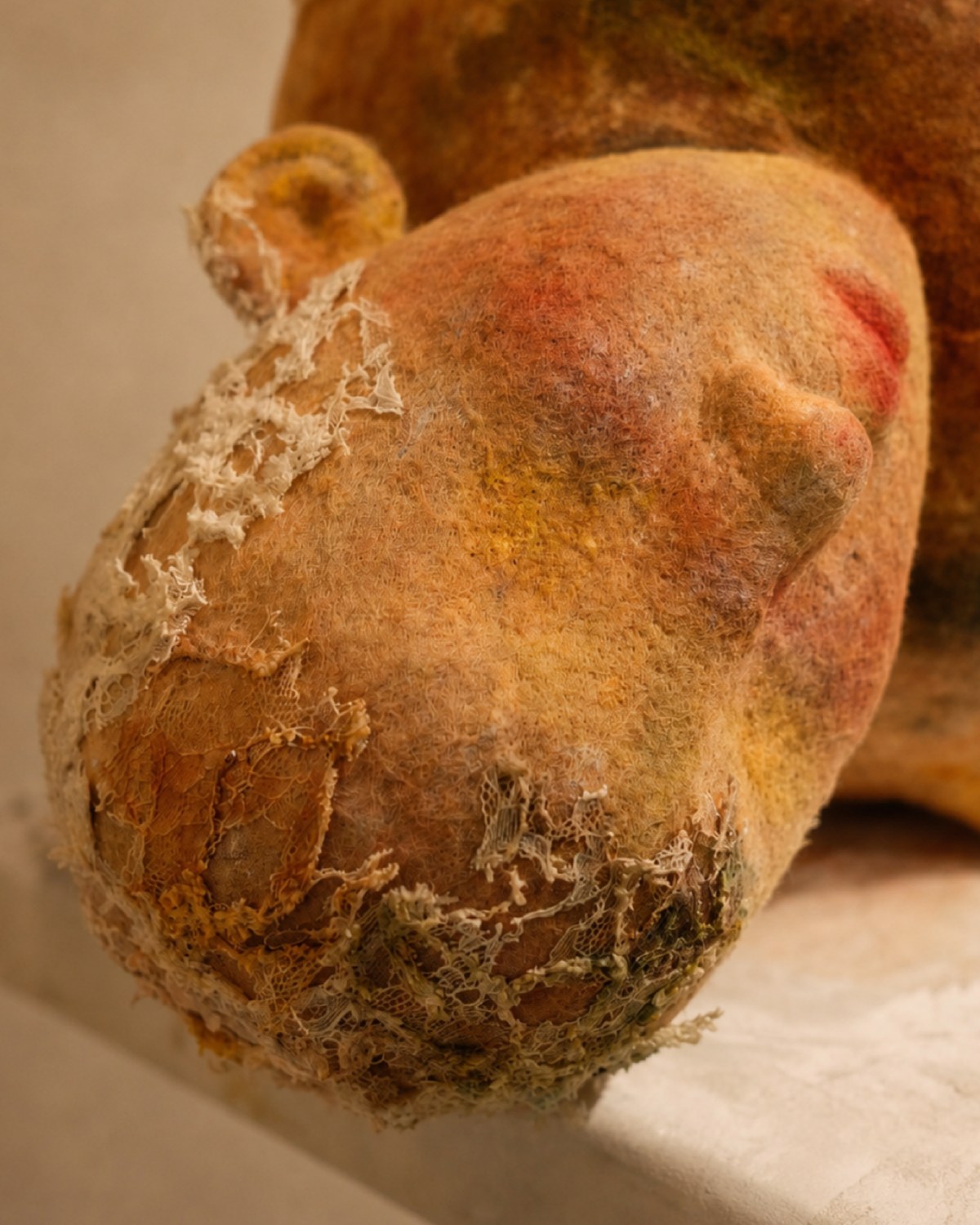 Head detail of Broken Jar showing a worn wool surface, closed eyes, soft scars, and textured handmade fibers.
