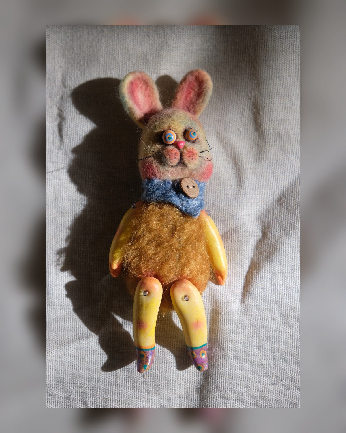Tick Tock handmade wool rabbit art doll lying in warm light with colorful eyes and yellow legs.