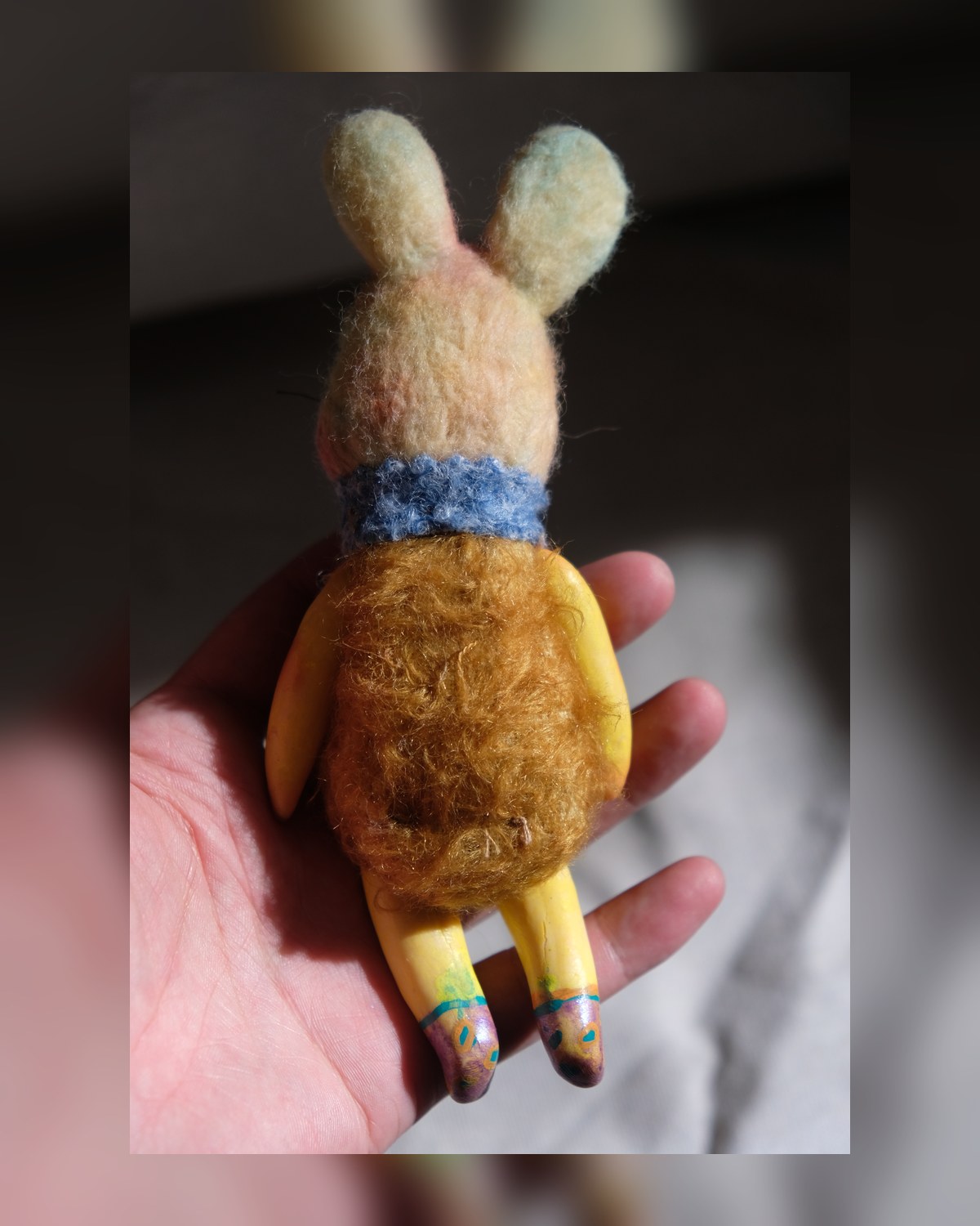 Back view of Tick Tock showing the brown wool body, pale rabbit ears, blue collar, and yellow legs.