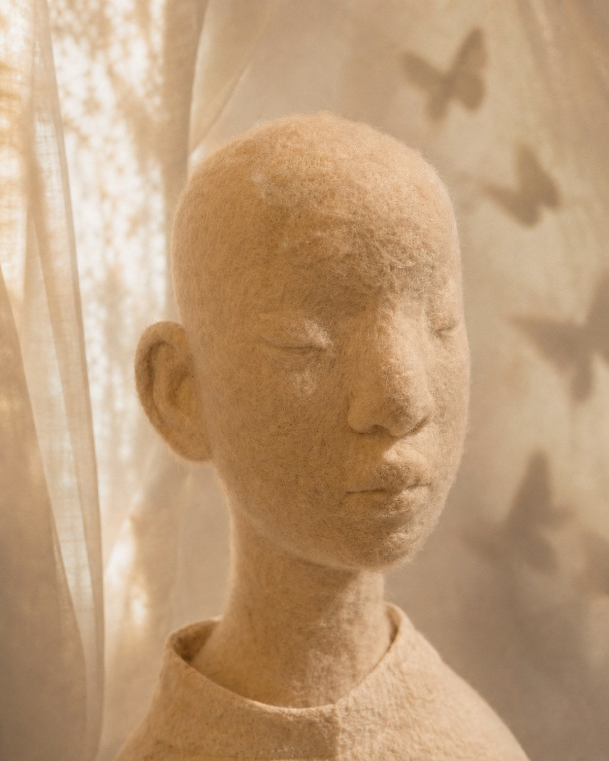Portrait detail of Zhuang Sheng showing the hand-felted wool face, closed eyes, and soft butterfly-shadow atmosphere.